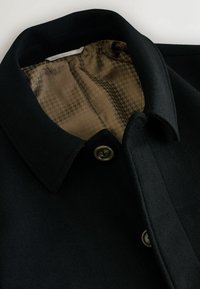 Schwarzer Wollmantel mit einem strukturierten braunen Hahnentrittmuster-Futter, ausgestattet mit einem klassischen Kragen und einem Knopfverschluss. Glatte Außenoberfläche.