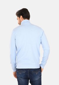 Maglione turchese a collo alto realizzato in tessuto lavorato a maglia, con maniche lunghe e colletto a coste. Indossato con jeans in denim scuro.