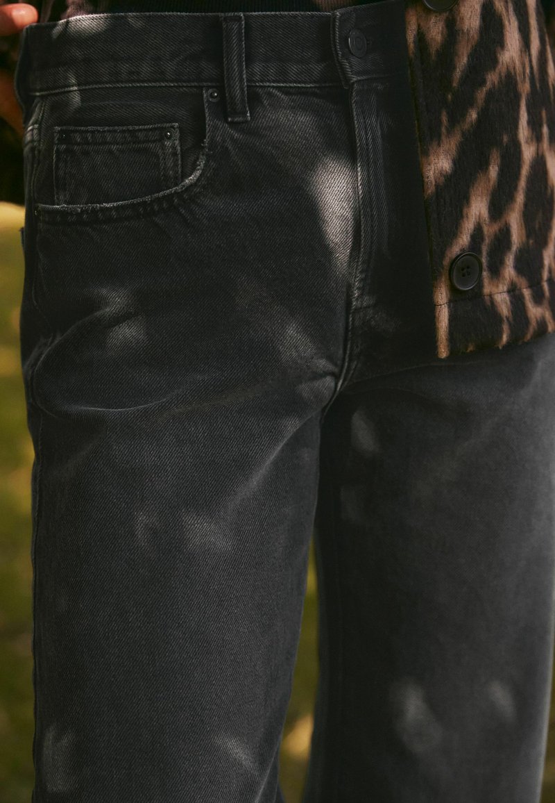 Jeans de mezclilla negra con una textura ligeramente desgastada, que cuentan con un pequeño bolsillo trasero y un diseño elegante, combinados con una chaqueta de estampado de leopardo.