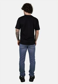 T-shirt nera in cotone, maniche corte, girocollo; abbinata a jeans denim azzurri chiari, slim fit, tasche posteriori visibili, indossata con sneakers nere.