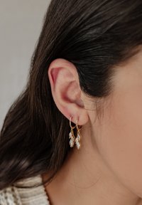 Goldene Ohrhänger mit klaren, marquiseförmigen Edelsteinen, die an zarten Ketten hängen und eine glänzende Oberfläche sowie filigrane Designdetails zeigen.