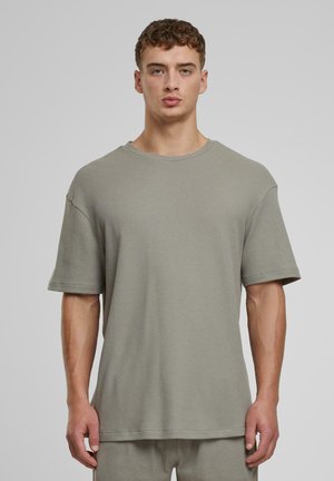 T-shirt à manches courtes, coupe ample, dans un vert olive discret, fabriqué en tissu texturé avec un motif côtelé. Col rond avec des manches roulées.
