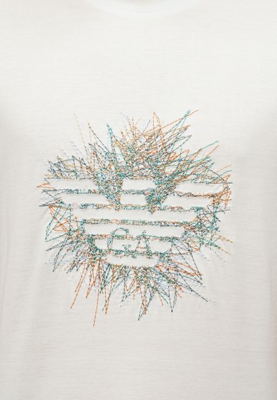 Κέντημα με πολύχρωμες κλωστές που σχηματίζει μια αφηρημένη ακτινοβόλο αστέρι γύρω από ένα οριζόντιο λογότυπο με ρίγες σε φωτεινό υφασμάτινο φόντο.