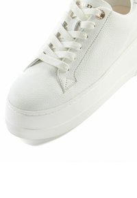 Baskets blanches avec un cuir texturé, des lacets plats, un design perforé sur le côté et une semelle blanche épaisse avec un minimum de détails.