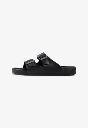 Schwarze Sandalen mit zwei verstellbaren Riemen und grauen Beschlägen, aus strukturiertem Material gefertigt. Die Sohle ist flach und weist ein dezentes Profil auf.