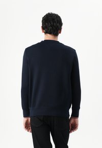 Sweatshirt azul marinho com mangas longas, punhos e bainha canelados, textura suave, detalhe de cor subtil nos punhos, design minimalista.