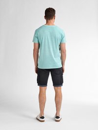 T-shirt azzurro a girocollo, maniche corte, abbinato a pantaloni cargo scuri con orli arrotolati e sneakers bianche con dettagli neri.