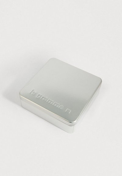 Cutie rectangulară din metal argintiu, cu colțuri rotunjite și text gravat "le gramme" pe capac.