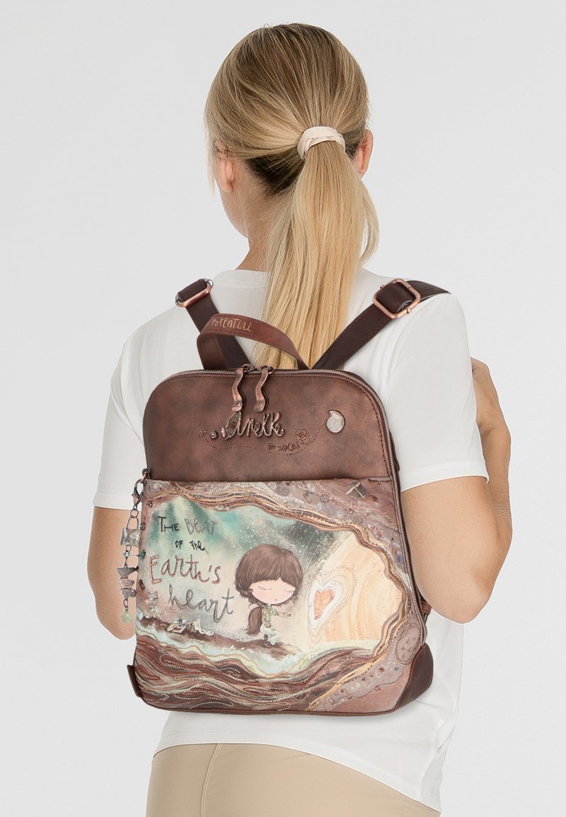 Brauner Rucksack mit einer fantasievollen Illustration eines Kindes und dem Satz "Der Schlag des Herzens der Erde", mit dekorativen Reißverschlussanhängern.