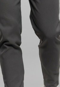 Pantalons gris foncé en tissu lisse et texturé avec une coupe fuselée. Présente des détails de couture subtils et une taille élastique.