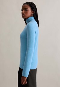 Light blue ribbed turtleneck sweater with long sleeves, fitted design, and soft texture; worn with a simple black skirt.