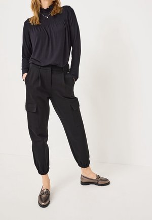 Zwart langarmshirt met geplooide details bij de halslijn, gecombineerd met zwarte cargobroek met elastische manchetten en twee zijzakken.