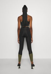 Reggiseno sportivo nero e leggings con accenti verde oliva. I leggings presentano una texture liscia e un design aderente. Scarpe da ginnastica nere completano il look.