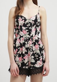 Svart blommig rompers med rosa och gröna blommönster, tunna axelremmar, figursydd midja och spetsdetaljer i nederkanten. Lätt tygstruktur.