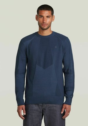 Pull en tricot bleu marine avec des motifs texturés, encolure ronde et poignets côtelés. Il présente une coupe ajustée et une silhouette décontractée.
