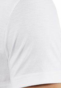 T-shirt bianco in cotone con maniche corte, caratterizzato da una texture liscia e un collo rotondo, con un dettaglio di cucitura vicino alla spalla.