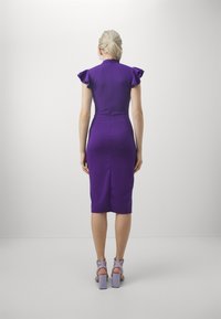 Rochie violet ajustată, cu mâneci volan, tăietură până la genunchi, fermoar la spate și textură fină. Asortată cu sandale cu toc pătrat de un violet deschis.