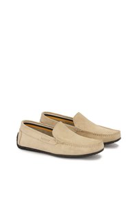 Bež semiš loafers s slip-on oblikom, kontrastnim šivanjem in črnimi gumijastimi podplati. Notranjost ima rumeno-črto podlogo.