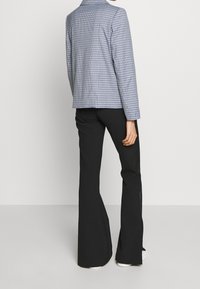 Blå och vit rutiga långärmad blazer, i kombination med svarta utsvängda byxor. Blazern har en slagkrage och rak passform.