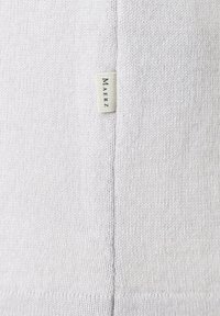 Hellgrauer Strickpullover mit weicher Textur, ausgestattet mit einer Nähdetail und einem kleinen Markenschild, das an der Seite angenäht ist.