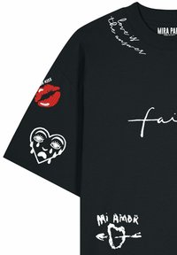 T-shirt noir avec texte manuscrit blanc « l'amour est la réponse », lèvres rouges avec « Mon baiser » sur la manche, cœur qui pleure, et « Mi Amor » avec des graphismes de flèches.