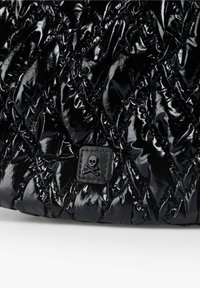 Tejido de quilt negro brillante con un pequeño parche cuadrado que presenta un emblema de calavera y tibias cruzadas cosido en el centro.