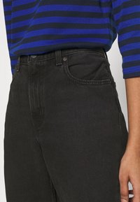 Jeans de mezclilla negra con cintura alta y bolsillos laterales, combinados con una blusa a rayas en azul y marino con mangas tres cuartos.