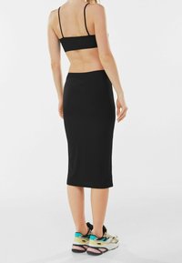 Svart kroppsnära tvådelat set bestående av en croppad topp med tunna band och en midilång kjol. Matchat med flerfärgade sneakers.