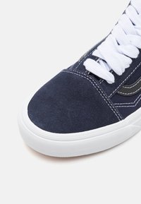 Marinblå mockaskor med vita snören, gummisula och kontrasterande grå sidodetaljer. Har sydda detaljer på hälen och tån.