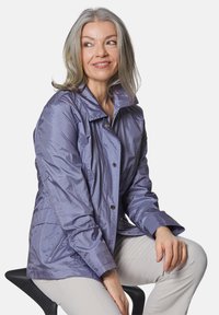 Leichte lila Jacke mit glänzender Textur, mit Kragen, vorne mit Knöpfen zu schließen und zwei Seitentaschen. Einfaches Design.