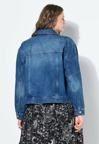 Jeansjacka i mellanblått med en klassisk passform, som har en spetsig krage och knäppte manschetter. Texturerad tyg med subtila blekningar.