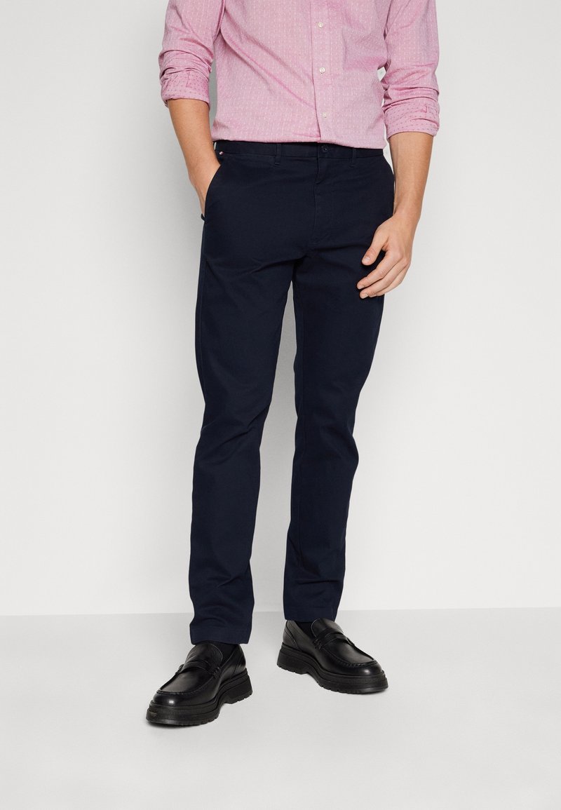 Chino blu navy realizzati in cotone, con una vestibilità slim, tasche laterali e una texture liscia. Indossati con una camicia a fantasia e scarpe nere.