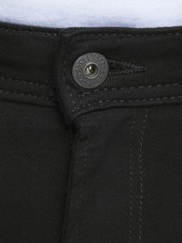 Jeans de denim negro con cierre de botón metálico, costuras visibles y una tela suave y texturizada. Marcado distintivo de la marca en el botón.
