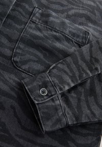 Camicia nera con un motivo a strisce di tigre sottile, colletto con bottoni e una tasca sul petto con bottone abbinato. Tessuto strutturato.