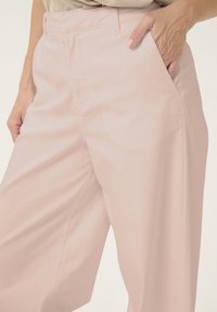 Bledosivé široké nohavice vyrobené z bavlnenej zmesi, s bočnými vreckami a hladkou textúrou, so rovnými pásmi a diskrétnym prešívaním.