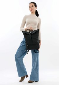 Der schwarze Rucksack verfügt über ein Rolltop-Design, verstellbare Träger und eine vordere Reißverschlusstasche. Hergestellt aus strapazierfähigem Stoff mit glatter Textur.