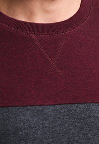 Sudadera color bloqueada en burdeos y gris oscuro con cuello redondo, que presenta costuras visibles y un tejido suave y texturizado.