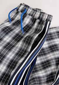 Pantalon à carreaux noir et blanc avec une ceinture élastique, des cordons de serrage bleus et des bandes latérales comprenant des accents bleus, blancs et noirs.