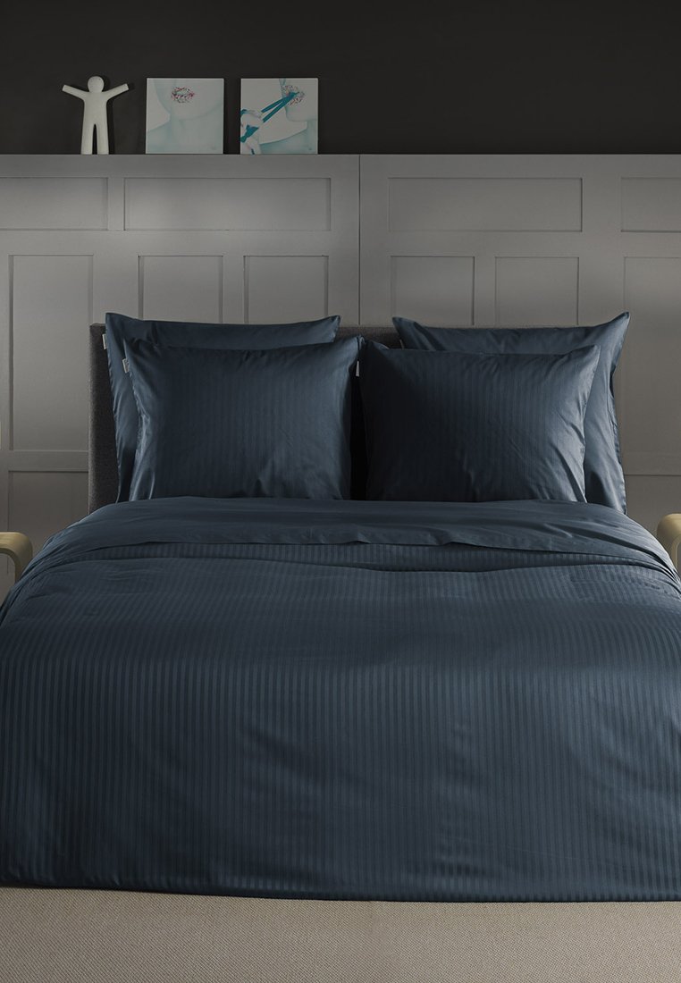 Navy niebieski zestaw pościeli w paski z dwiema pasującymi poszewkami na poduszki i teksturowaną kołdrą, wyeksponowany na nowoczesnym łóżku na neutralnym tle.