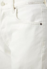 Jeans de denim blancos con una textura suave, costuras visibles y un bolsillo frontal con un acento de remache metálico.