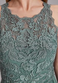 Grünes besticktes Kleid mit aufwendigen Blumenmustern, Perlenakzenten und einem transparenten Overlay am Ausschnitt und Oberteil.