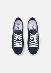 Tmavě modré síťové tenisky s bílými tkaničkami a gumovými podrážkami. Mají značkové stélky, texturovaný síťový svršek a klasický nízký design.