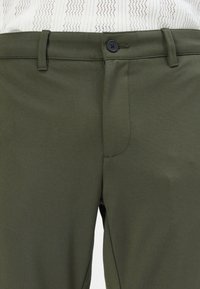 Pantalones de color verde oscuro, hechos de un material suave, con cierre de botón, trabillas para cinturón y un diseño liso y ajustado.