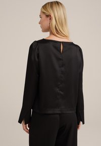 Blusa nera con texture a righe verticali, chiusura a chiave sulla schiena, maniche lunghe a sbuffo con polsini a fessura e silhouette elegante.