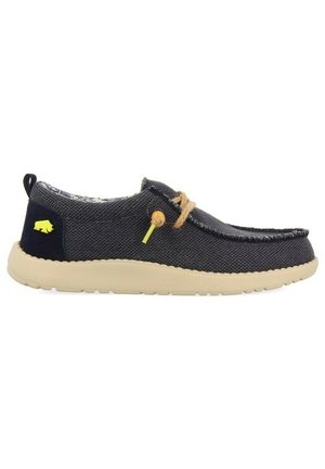 Zapatilla slip-on de lona azul marino con suela beige, cordones marrones y un detalle de logo en amarillo. Presenta una puntera redonda y un diseño de tela texturizada.