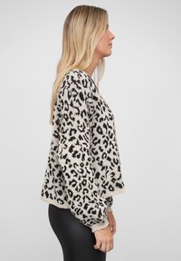 Strikkegenser i beige med svart leopardmønster, med en avslappet passform, rund hals og ribbestrikkede ermer. Glatt tekstur.