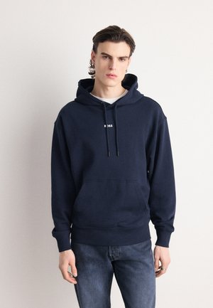 Marineblauwe katoenen hoodie met een voorzak, capuchon met trekkoorden en een wit logo. In combinatie met donkere denim jeans. Soepele textuur.