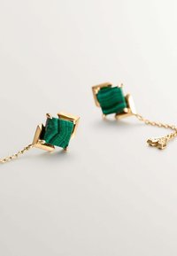 Pendientes de oro con piedras cuadradas de malaquita con patrones de rayas verdes, conectados por una delicada cadena de oro con un detalle de acento.