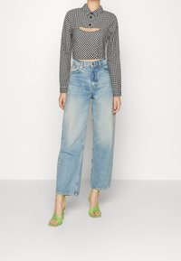 Černobílá kostkovaná zkrácená košile s límečkem a výřezem. Světle modré džíny s vysokým pasem a rovnými nohavicemi. Zelené sandály na podpatku.