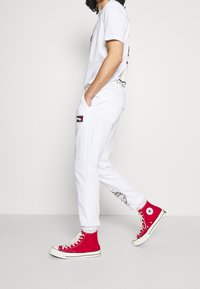 Vit bomullströja och matchande joggingsbyxor med sidofickor och svarta grafiska detaljer. Röda hög-top canvas sneakers kompletterar outfiten.